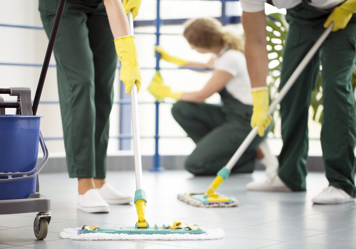 Coworkers moping a floor and a woman dusting a railing in an office